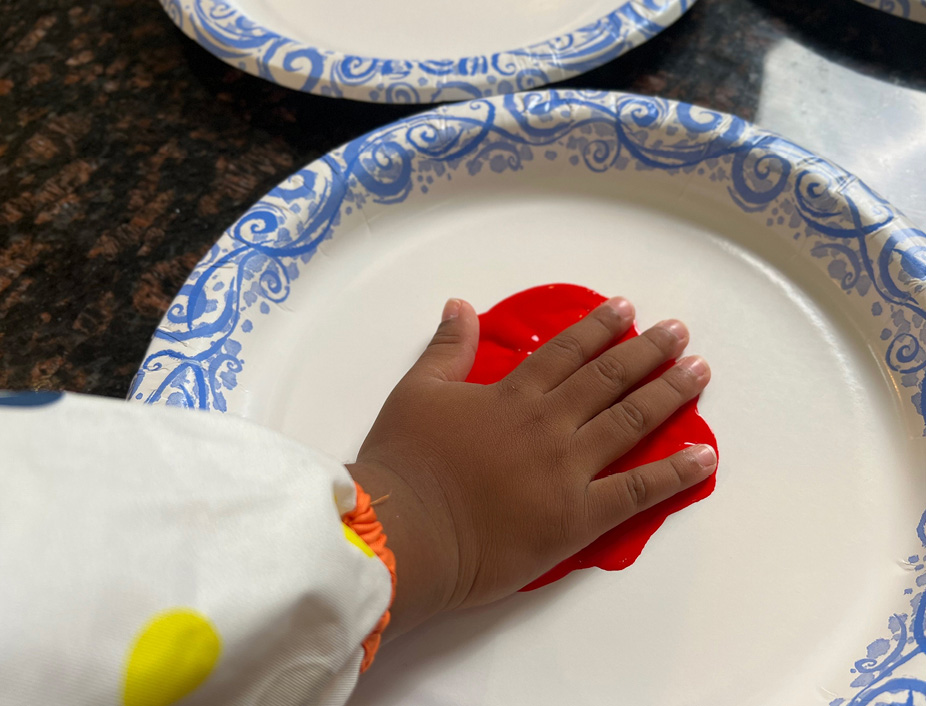 Child placing their full hand, palm facing down, in red finger paint